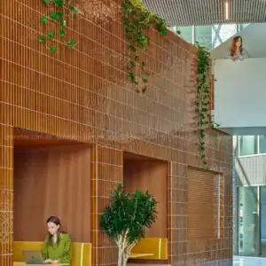 Không gian thương mại sử dụng gạch thẻ màu nâu caramel men bóng 50x200 mm ốp tường và cột, kết hợp cây xanh tạo phong cách kiến trúc hiện đại.