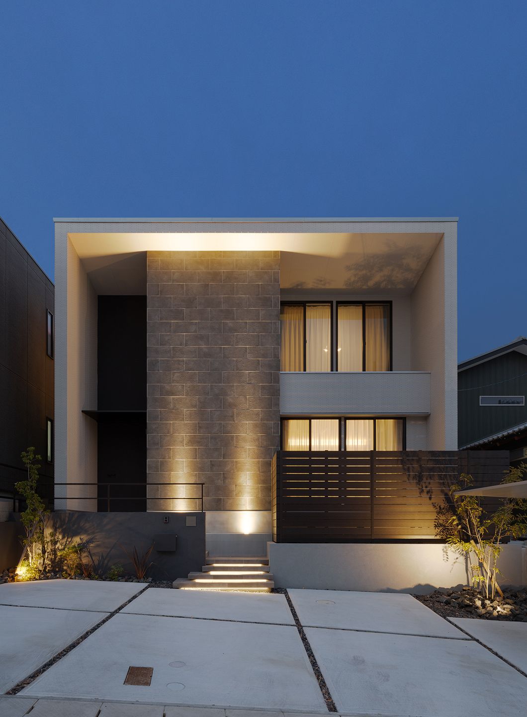 Kết hợp gạch xám với ánh sáng ngoại thất giúp nổi bật vân và chiều sâu vật liệu vào buổi tối.